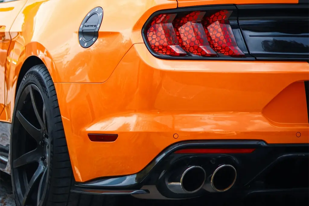 Rear bumper of an orange Ford Mustang with chrome quad exhaust tips